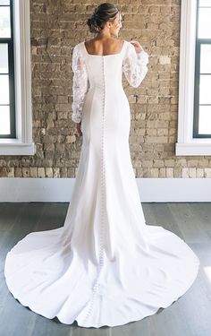 a woman in a white wedding dress standing by a brick wall with her back to the camera