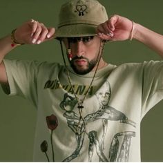 a man wearing a hat and holding his hands to his ears while standing in front of a green background