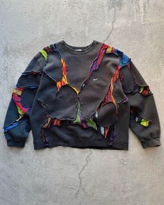 a black sweatshirt with multicolored birds printed on the front and back, sitting against a concrete wall