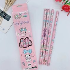 three pink pencils with hello kitty on them next to some flowers and a package