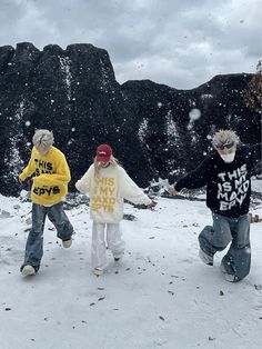 three young boys playing in the snow with their hands out and one boy wearing a yellow shirt