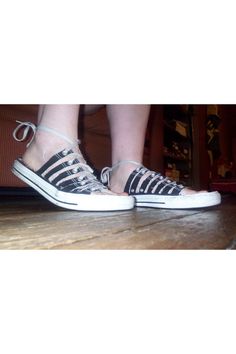 a person standing on top of a wooden floor wearing black and white striped converse shoes