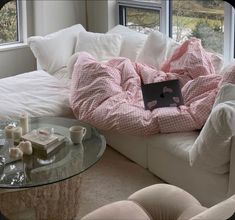 a laptop computer sitting on top of a couch covered in pink and white blankets next to a window