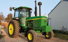 a large green tractor parked in front of a white building with yellow rims on it's tires