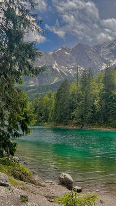 a lake surrounded by trees and mountains under a cloudy sky