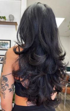 the back of a woman's head with long black hair and tattoos on it