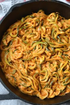 a skillet filled with noodles and sauce on top of a table cloth next to an apple