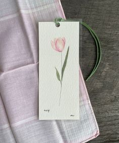 a card with a pink flower on it next to a green string and a piece of paper