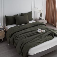 a bed with green sheets and pillows in a white room next to a table with a lamp on it