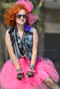 a woman with red hair wearing a pink tutu skirt and denim jacket, sunglasses and bracelets