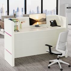 an office desk with a computer monitor and phone on it in front of large windows