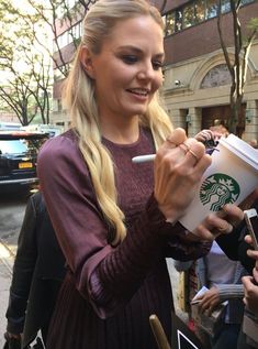 a woman holding a starbucks cup in her right hand and talking to someone on the other side