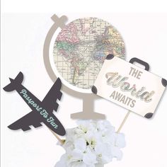 the world awaits sign with an airplane and map on it next to a bouquet of flowers