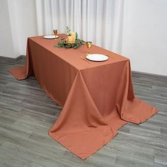 an orange table cloth on top of a wooden floor next to two plates and wine glasses