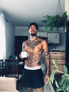 a man with tattoos standing in a living room next to a table and planter