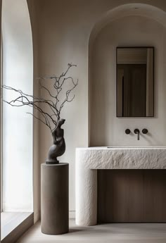 a vase with branches in it sitting next to a sink and mirror on the wall