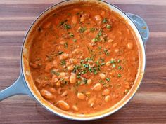 a pot filled with beans and garnish on top of a wooden table