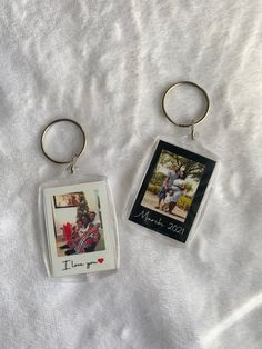 two key chains with pictures attached to them sitting on a white cloth covered bed sheet