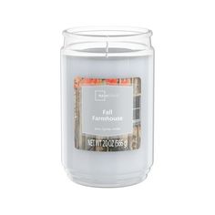 a white candle with an orange label on the front and bottom, in a clear glass container