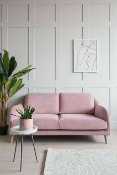 a pink couch sitting next to a potted plant on top of a white table