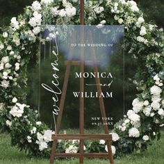 an easel with white flowers and greenery around it is the backdrop for a wedding ceremony