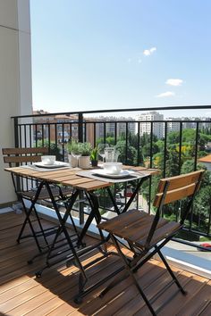 A small balcony with wooden folding table and chairs, offering a cozy seating arrangement amidst a high-rise view, perfect for small outdoor space. Apartment Decorating Balcony, Balcony Seating, Small Apartment Balcony, Decorating Balcony, Balcony Table, Balcony Chairs, Seating Ideas