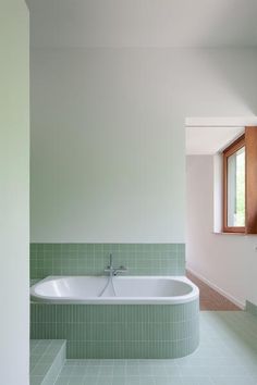 a bathroom with green tiles and a white bathtub in the middle of the room