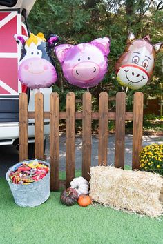 three farm animal balloons are on display in front of a fence with hay and pumpkins