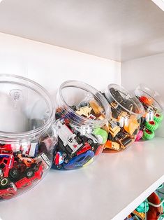 several plastic containers filled with toy cars on top of a white shelf in a room