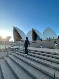 a woman is walking up some steps in front of the sydney opera house at sunset