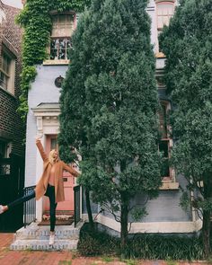 a woman standing on steps in front of a building with trees and bushes around her