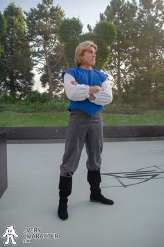 a man standing with his arms crossed in front of him, wearing boots and a blue shirt