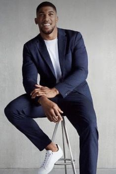 a man sitting on top of a stool wearing a blue suit and white sneakers with his hands in his pockets