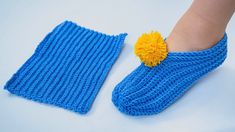 a pair of blue knitted slippers with a yellow pom - pom