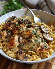 a bowl filled with pasta and mushrooms on top of a wooden table next to a fork