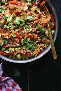 a bowl filled with rice, beans and veggies next to silverware on a black surface