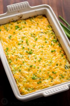 a casserole with cheese and green onions in a white dish on a wooden table