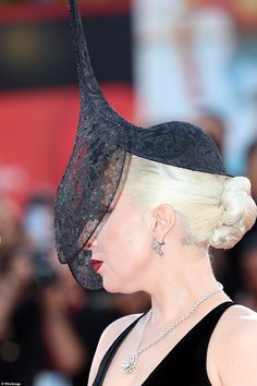 lady with white hair wearing black hat at red carpet event in front of large crowd