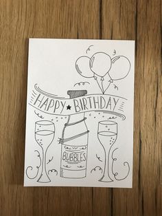 a birthday card with bubbles and balloons on it, sitting on a wooden table next to a bottle of booze