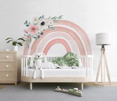 a baby's room decorated in pastel colors with a rainbow mural and teddy bear