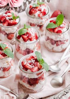 strawberry shortcakes with whipped cream and mint leaves in glass jars on a tray