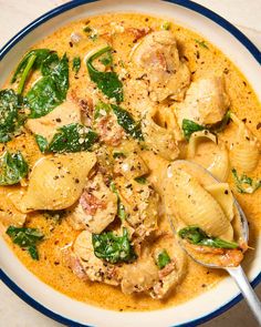 a white bowl filled with pasta and spinach covered in sauce on top of a table