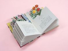 an open book with flowers on it sitting on top of a pink table next to a pair of scissors