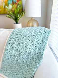 a crocheted blanket sitting on top of a white couch next to a lamp