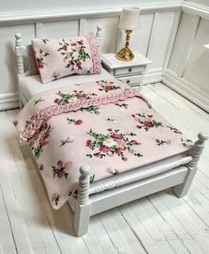 a white bed with pink flowers on it in a room next to a night stand