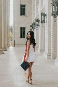 a woman in a white dress is holding a black and red purse while posing for the camera