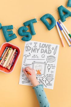 a child's hand writing on a paper next to some crayons and colored pencils