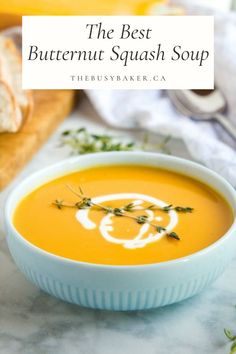 a bowl of butternut squash soup on a marble table with bread in the background