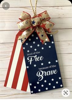 a patriotic gift bag hanging from a string on a white wooden background with the words land of the free because of the brave written in red, white and blue