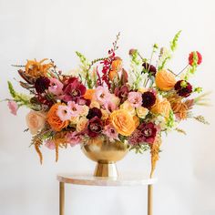 a gold vase filled with lots of different colored flowers on top of a white table